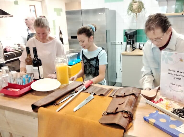 Bar in de keuken met drankjes, messen op een rol en gasten aan de counter.