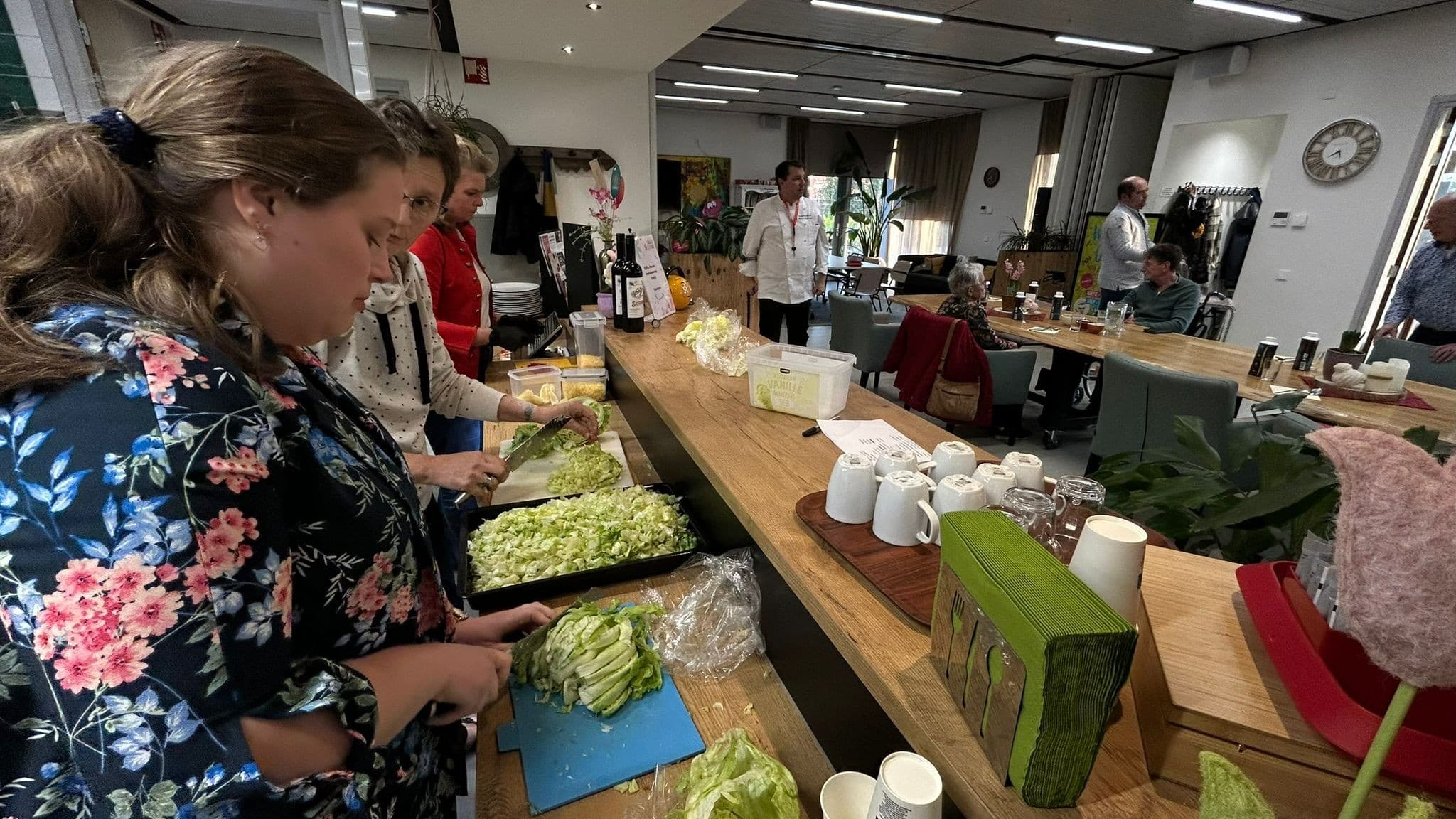 Mexicaanse avond: voorbereiding van sla en garnering; gasten aan tafel op de achtergrond.