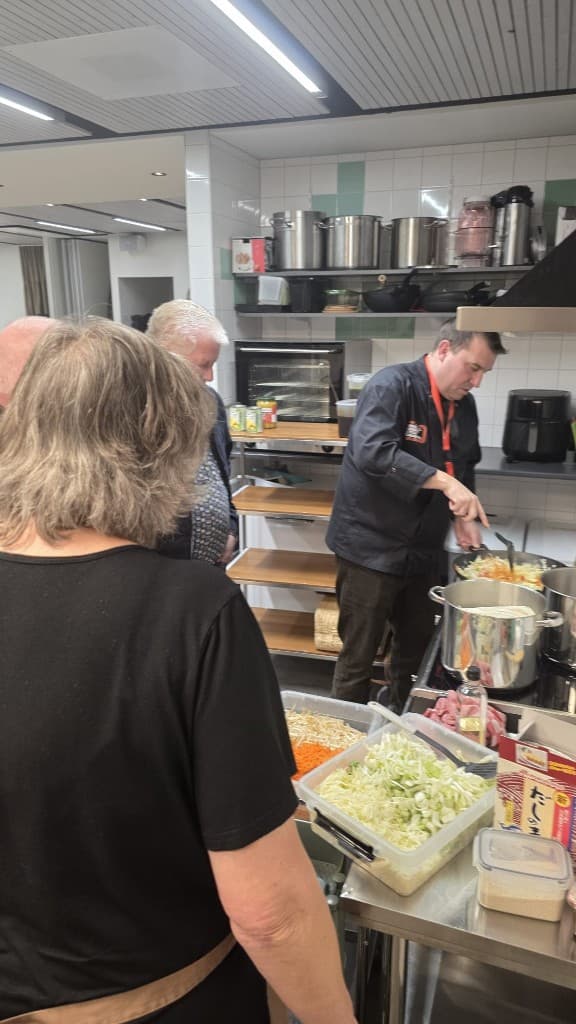 Oosterse avond: chef kookt aan het fornuis terwijl deelnemers meekijken; voorbereide groenten en oosterse ingrediënten op de werktafel.